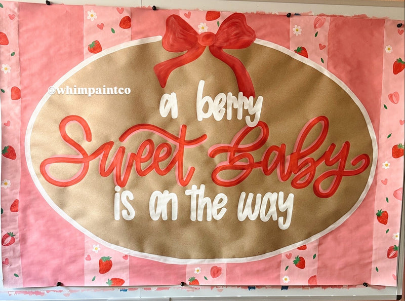 Paint banner sign with 'a berry sweet baby is on the way' text and a red bow on a pink background.