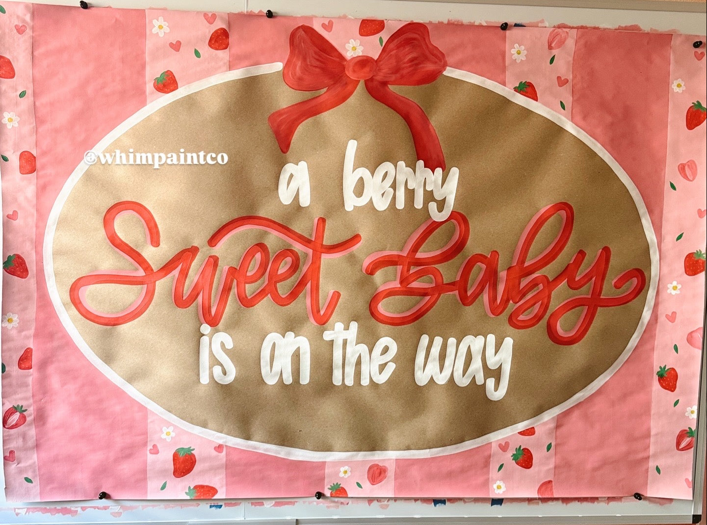 Paint banner sign with 'a berry sweet baby is on the way' text and a red bow on a pink background.